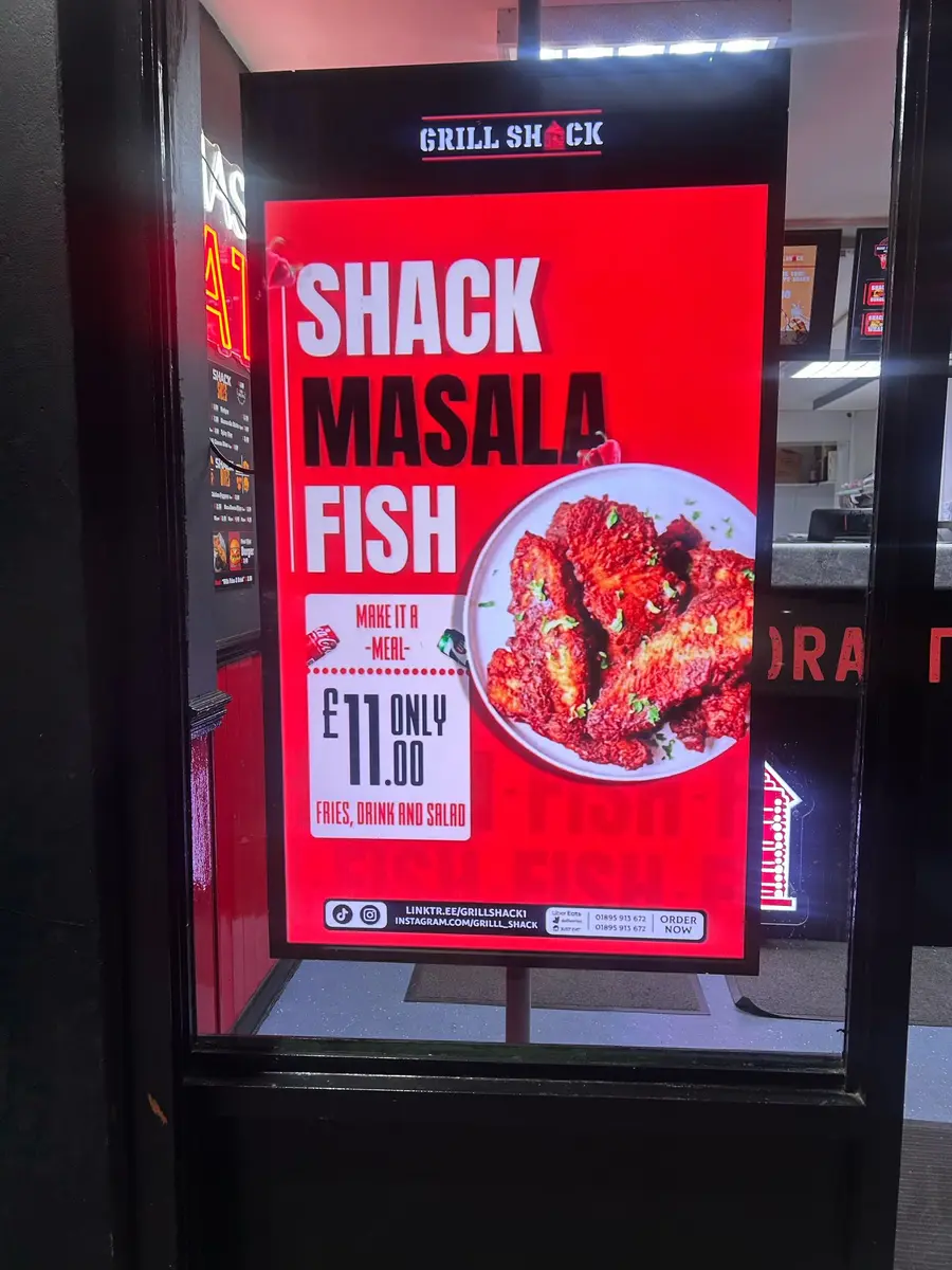 Digital menu board in a UK takeaway showing meal deals and prices.